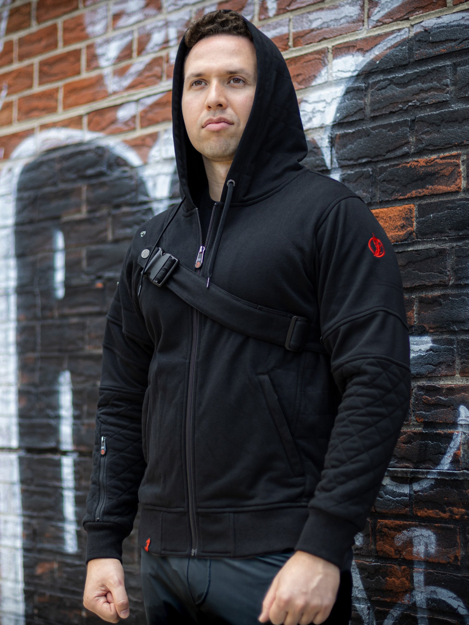 Model wearing Warrior Hoodie by Patch Notes Apparel at a 45-degree angle, highlighting the left sleeve’s padded quilting, chest belt, embroidered logo on the shoulder, right sleeve zip pocket, and custom main zipper.
